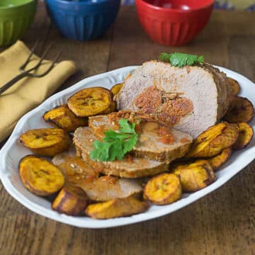 A photo of Cuban boliche on a white platter with fried plantains on the side.