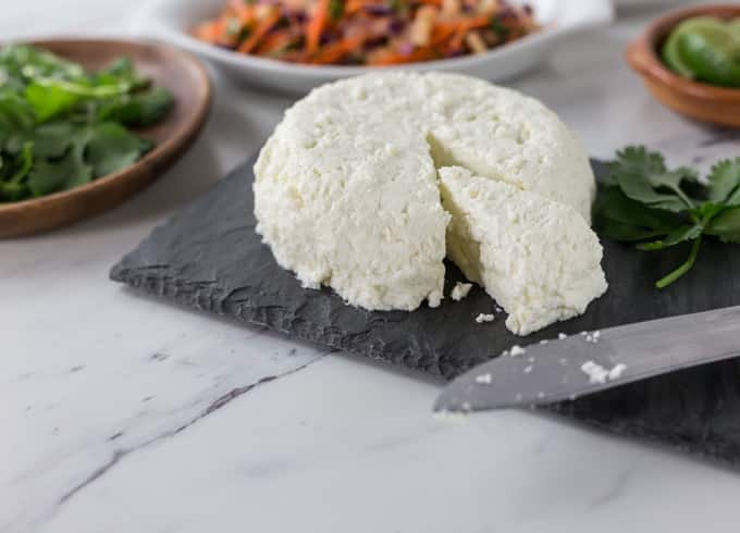 a round of homemade cheese on a slate with a plate of cilantro on the left