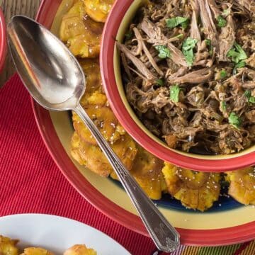 A photo of ropa vieja in a striped bowl with tostones on the side.