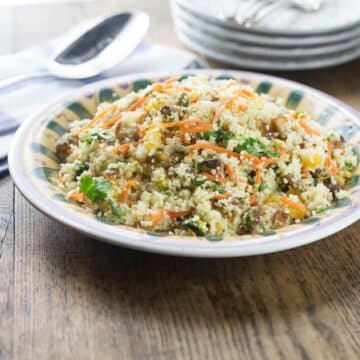 Couscous salad with dates, nuts and apricots on a plate with plates in the background.